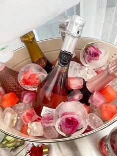 two bottles of champagne and some ice cubes in a bowl with flowers on the table