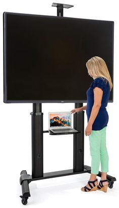 a woman standing in front of a tv with a laptop computer on it's stand