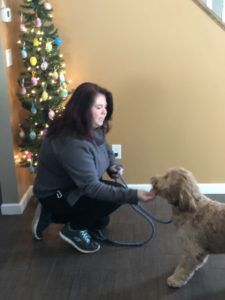 a woman kneeling down with a dog on a leash in front of a christmas tree