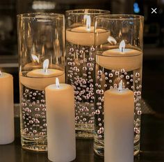 some candles are sitting in glass vases on a table with water and beads around them