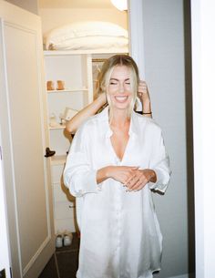 a woman standing in front of a closet holding her hair up to her head and smiling