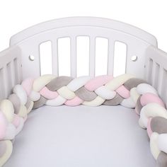 a white crib with pink, grey and white pillows on it's sides