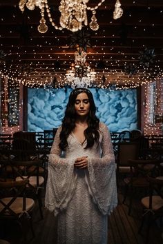 a woman standing in front of a chandelier with lights hanging from the ceiling