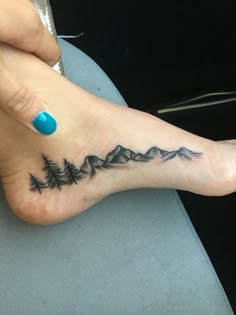 a woman's foot with a mountain and pine tattoo on her left side ankle