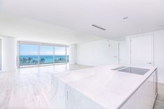 an empty kitchen with marble counter tops and white cabinets, overlooking the ocean from a high rise apartment