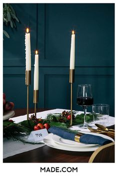 two candles are lit on a table with place settings and fruit in the foreground