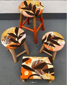 four wooden stools and one ottoman with leaves painted on the top, sitting in front of a white wall