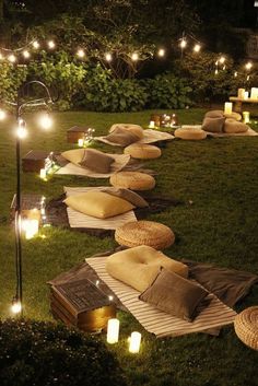 some pillows and lights are on the grass in front of an outdoor seating area with candles