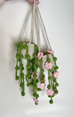 crocheted pink and green flowers hanging from hooks on the side of a white wall