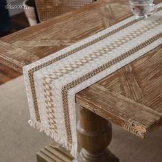 a wooden table topped with a white and brown table runner next to a glass filled with water