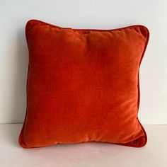 an orange velvet pillow on a white surface with no one in the photo to describe