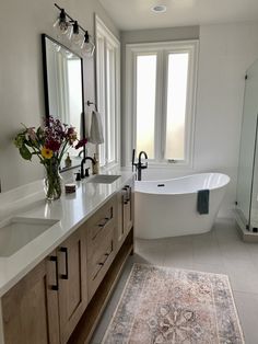 a bath room with a tub a sink and a rug on the floor in front of two windows