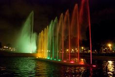 a colorful fountain is lit up at night time with bright lights on the water's surface