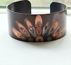 "This unique copper bracelet is made by painting patterns onto copper with a torch, and as the copper heats and cools it turns different colors naturally! Its quite an amazing process. the cuff is 1\" wide and is flexible enough so that you can make it fit your wrist. It is protected with a sealant to keep it from further oxidizing. These are custom made per order, so please keep in mind that with this process, nature is in charge of the colors, so see each one that I make is unique and cannot b Handmade Artistic Copper Bracelet, Handmade Artistic Copper Bracelets, Handmade Brown Copper Bangle, Handmade Copper Bangle In Brown, Handmade Unique Copper Bangle, Copper Cuff Bracelet Wearable Art Gift, Unique Handmade Copper Bangle, Brown Copper Cuff Bracelet As Gift, Wearable Art Copper Bangle Bracelets