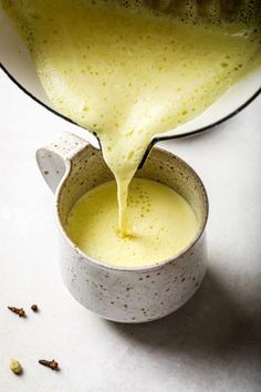 a pitcher filled with liquid sitting on top of a white counter next to a bowl