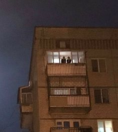 an apartment building at night with the moon in the sky and people standing on the balconies