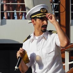 a man in a sailor's uniform holding a bottle and talking into a microphone