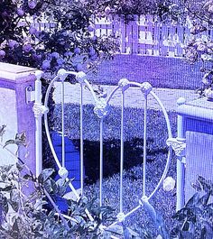 an iron heart shaped bed frame in the middle of some bushes and flowers with purple hues