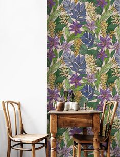 two wooden chairs sitting next to a table in front of a wall with flowers on it