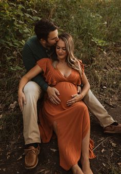 a pregnant couple cuddles while sitting on the ground