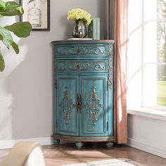 an ornate blue cabinet with flowers on top in front of a window and a potted plant