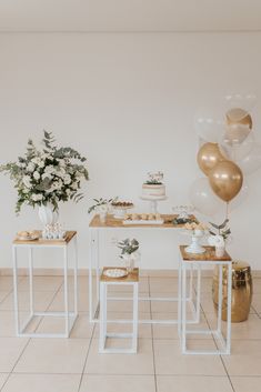 the dessert table is set up with gold balloons and white flowers in vases on top