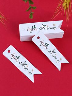 three white christmas gift tags sitting on top of a red table next to a plant