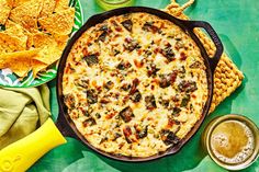 a pizza with cheese, olives and tortilla chips on a green table