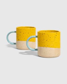 two yellow and white coffee mugs sitting next to each other on a gray background