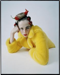 a woman in a yellow fur coat with red flowers on her head and hands behind her head