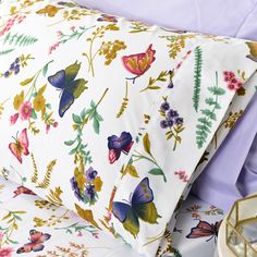 a bed with purple sheets and butterflies on it, next to a tray full of flowers