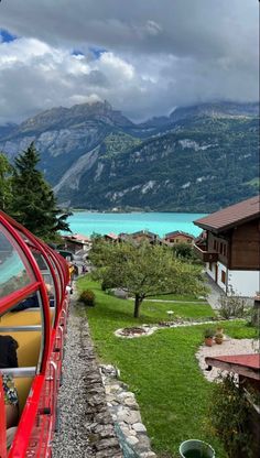 a red train traveling down tracks next to a lush green forest covered mountain side under a cloudy sky