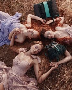 three beautiful women laying on the ground with their hair blowing in the wind and wearing dresses