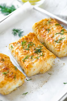 three fish fillets on a white plate with lemons and parsley in the background