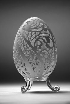 an intricately designed glass egg sitting on top of a metal stand in front of a gray background