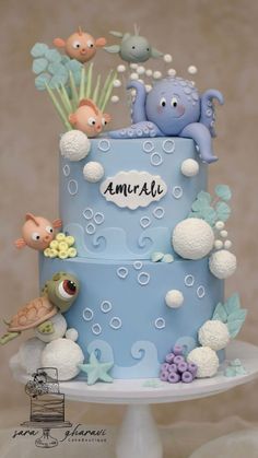 a blue cake with sea animals and bubbles on it's side, sitting on a white pedestal