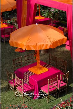 an orange and pink umbrella is on top of a table in the middle of some chairs