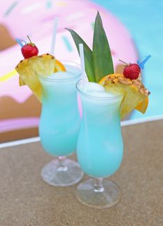 two glasses filled with blue liquid and topped with pineapple