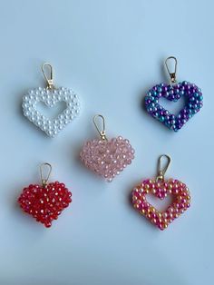 four heart shaped beaded charms sitting on top of a white table next to each other