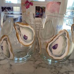 two glass cups sitting on top of a counter next to a book and flower vase