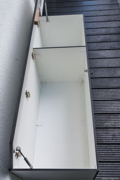 an open drawer on the side of a building that is white and has metal handles