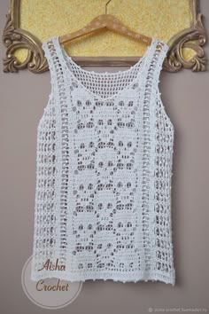 a white crocheted top hanging on a wooden hanger next to a mirror