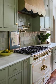 a kitchen with green cabinets and white counter tops, gold pulls on the stove top