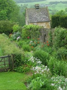 an old stone house surrounded by lush green grass and flowers in the foreground, with a wooden gate leading to it