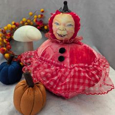 a red and white doll sitting next to two pumpkins