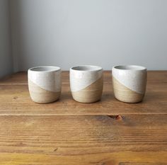 three white cups sitting on top of a wooden table