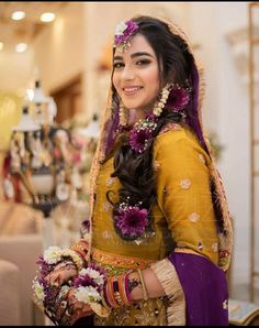 a woman in a yellow and purple outfit with flowers on her head smiles at the camera