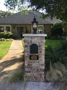 a brick mailbox sitting in front of a house with a lamp on top of it