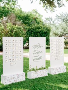 three white signs with flowers and greenery on them sitting in the grass next to each other