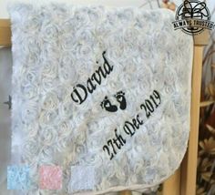 a white blanket with the name david and baby feet on it in black ink is hanging from a wooden frame